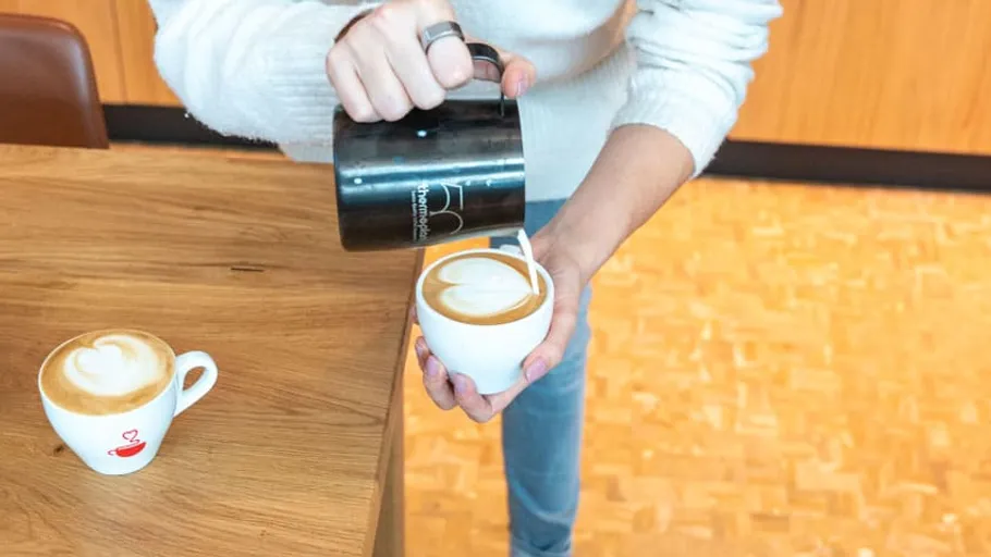 Person gießt Latte-Art in Kaffeetasse.