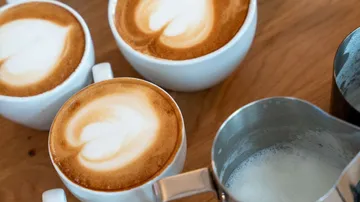 Cappuccinos mit Latte Art auf Holztisch.