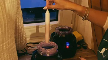 Hand dipping candle into hot wax machine.