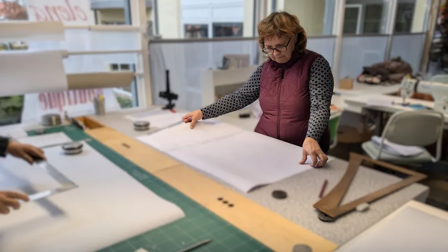 Woman measuring fabric on a worktable indoors.