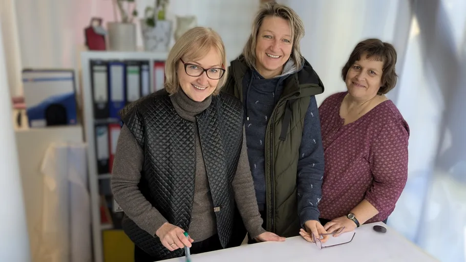 Three women smiling in an office setting.