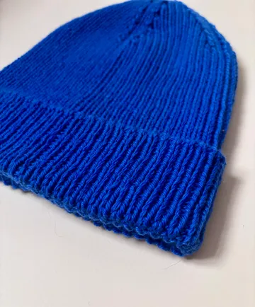 Blue knitted beanie on white surface.