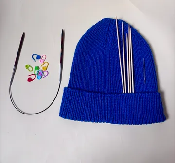 Blue knitted hat with knitting needles, markers