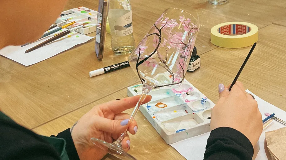 Person painting cherry blossoms on a wine glass.