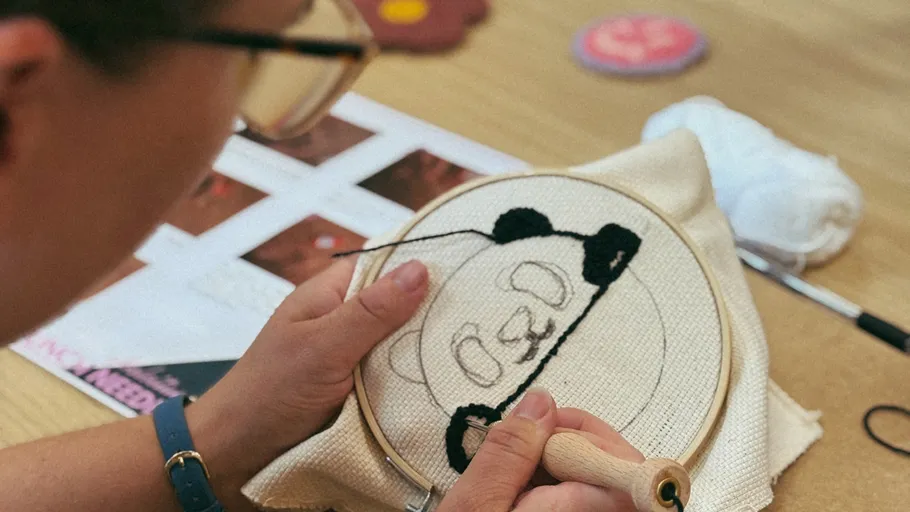Person embroidering panda design on fabric.