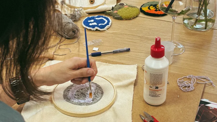 Person painting embroidery piece on table.