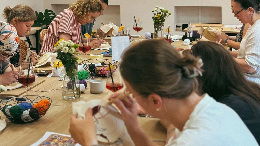 People embroidering at a table with drinks.