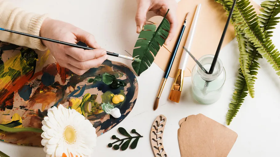 Hands painting leaf at bright workspace.