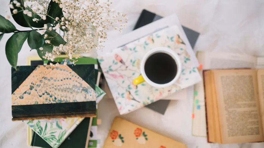 Coffee cup on floral notebooks, surrounded by books.