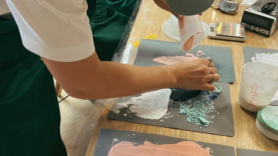 Person mixing colorful powders on a table.