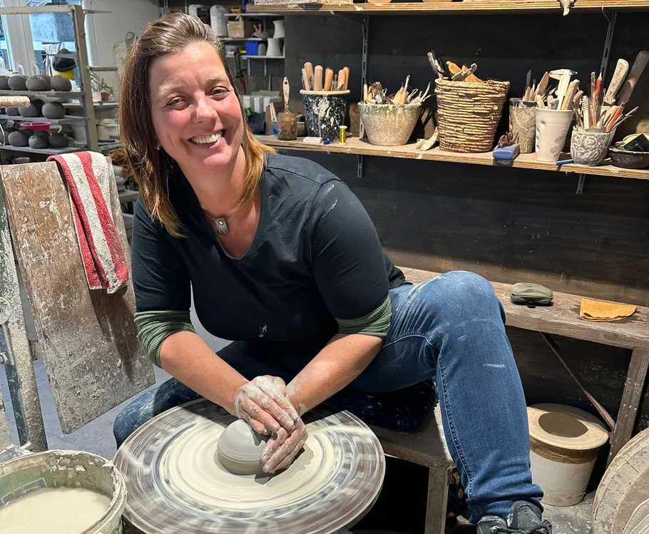 Woman shaping clay on pottery wheel in studio.