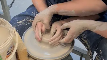 Hands shaping clay on a pottery wheel.