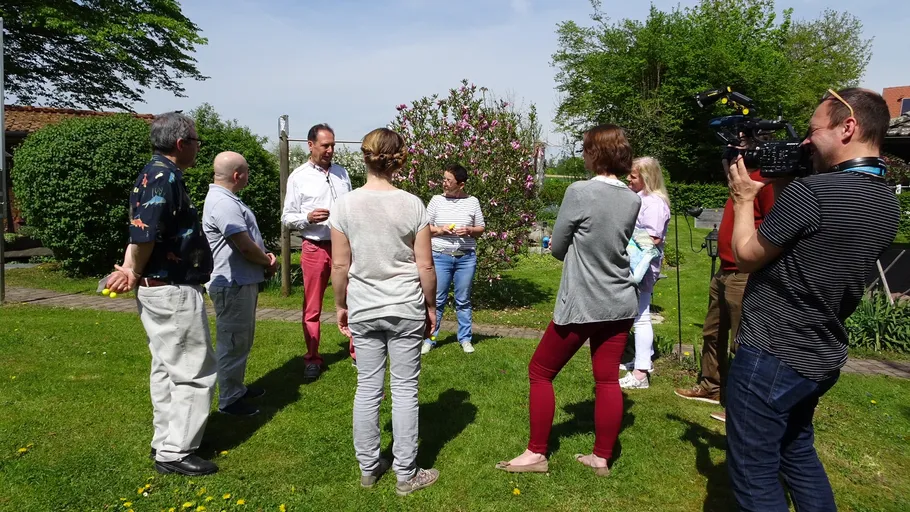 Gruppe diskutiert im Garten, Kamera filmt.