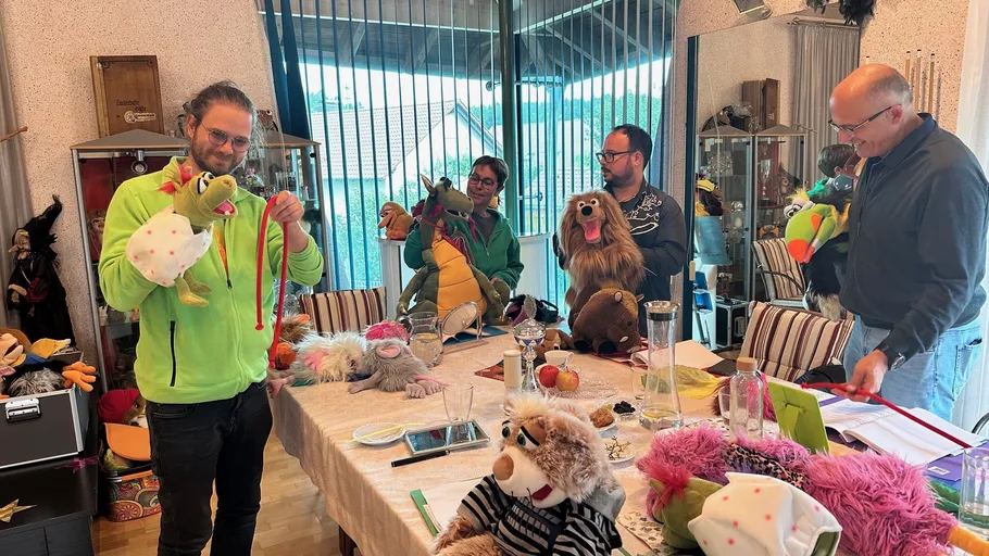 Four people use puppets around a table.