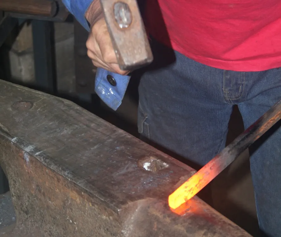 Blacksmith hammering hot metal on anvil.