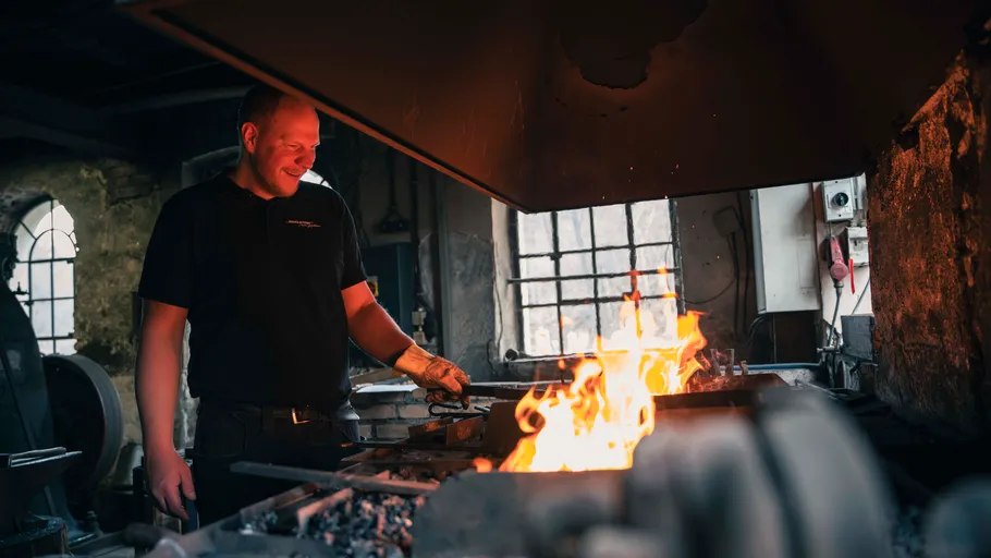 Blacksmith smiling near a forge in workshop.