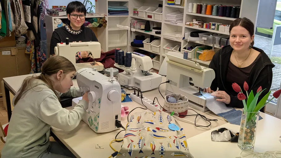 Three women sewing in a fabric shop.