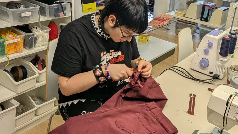 Person sewing red fabric in a workshop.