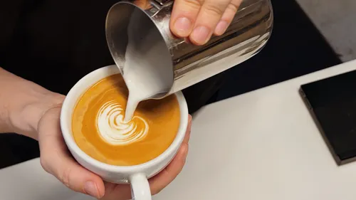 Barista pours milk creating latte art.