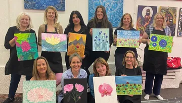 Gruppe von Frauen hält Gemälde drinnen.