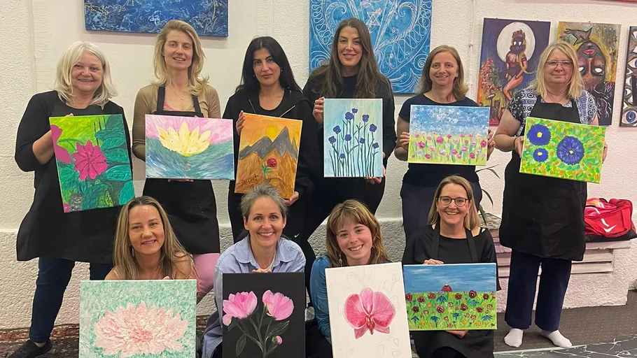 Gruppe von Frauen hält Gemälde drinnen.