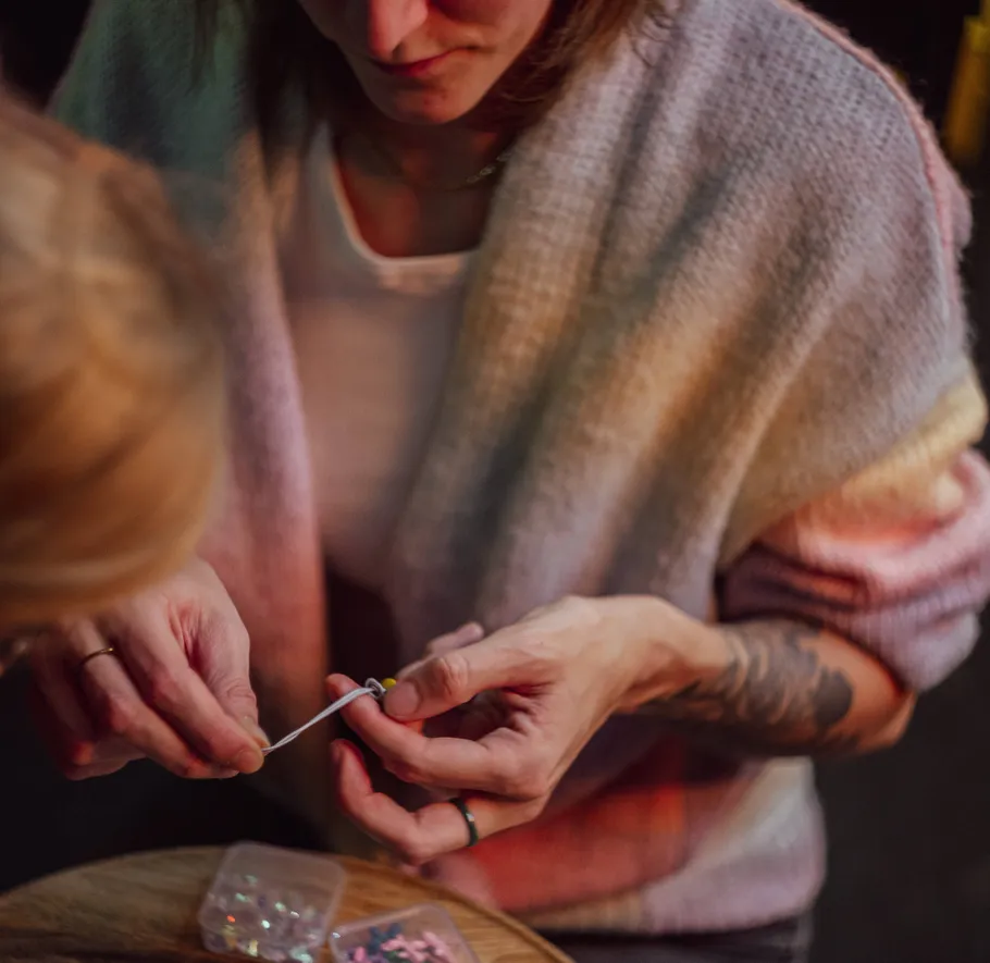 Person stringing beads at wooden table.