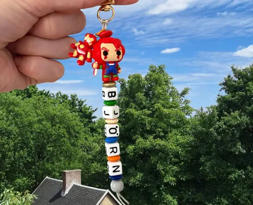 Hand holding keychain with figure above trees.