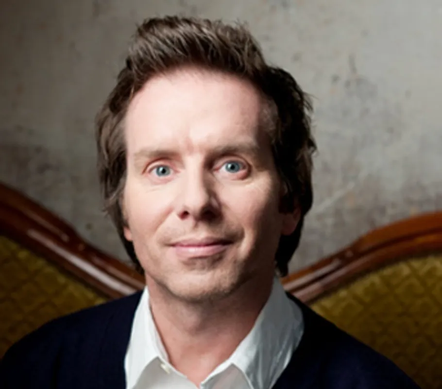 Man smiling, sitting on patterned couch.