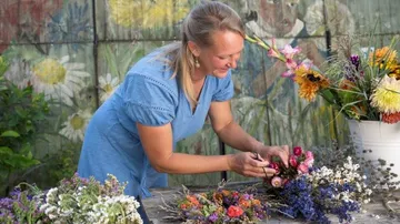 Woman arranging flowers on wooden table outdoors.