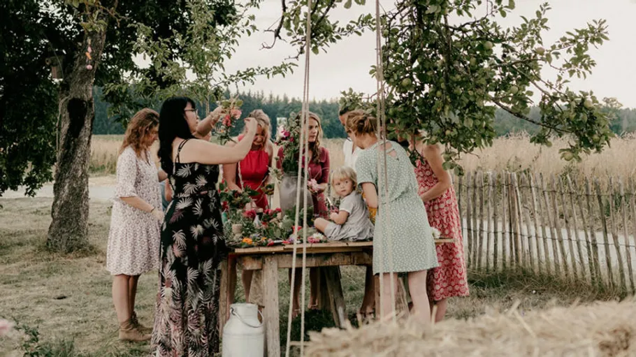 People gather around table outdoors, decorating with flowers.