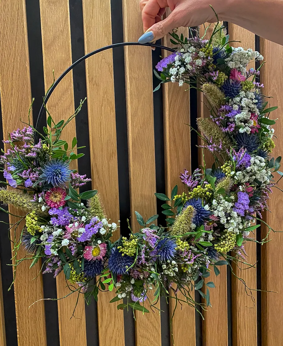 Hand hält Blumenkranz vor Holzhintergrund.