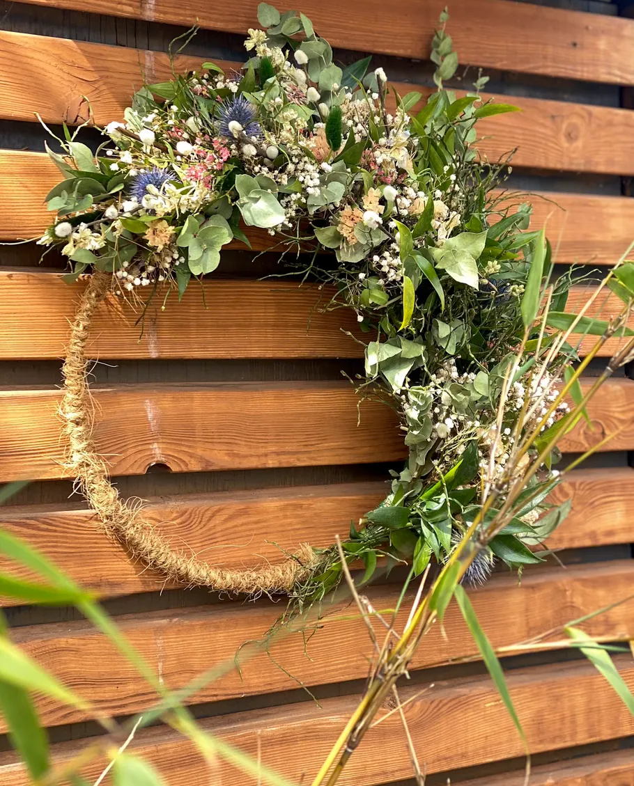 Floral wreath hung on wooden wall outdoors.