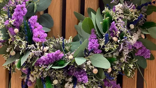 Hand holding floral wreath against wood wall.