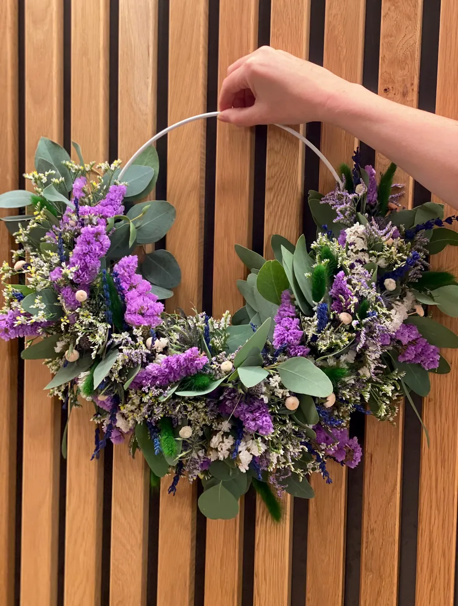 Hand hält Blumenkranz vor Holzwand.
