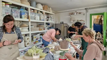 Five women make pottery in a creative studio.