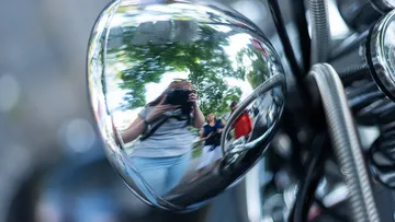 Reflection of photographer in chrome motorcycle part.