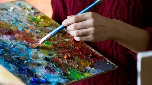 Hand holding paintbrush and palette indoors.