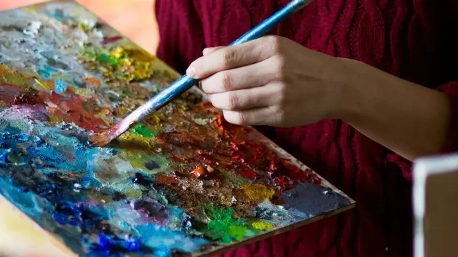 Hand hält Pinsel und Palette drinnen.