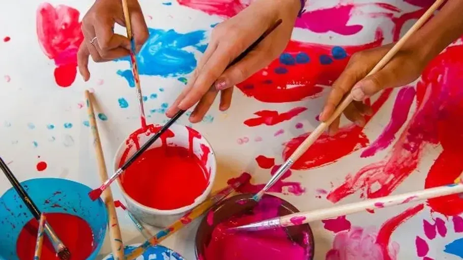 Hands painting with brushes on colorful paper.