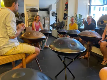 Gruppe von Menschen spielt gemeinsam auf Handpans in einem Raum.