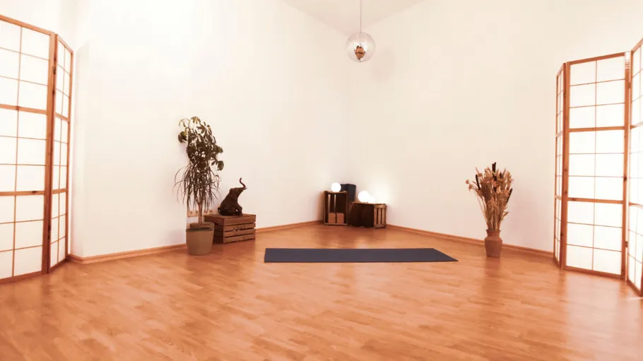 Empty yoga studio with a mat, wooden floor.