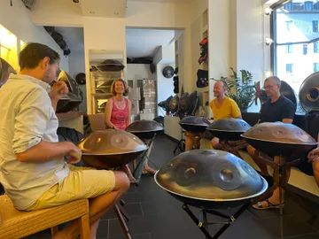 People play hang drums together in a bright room.