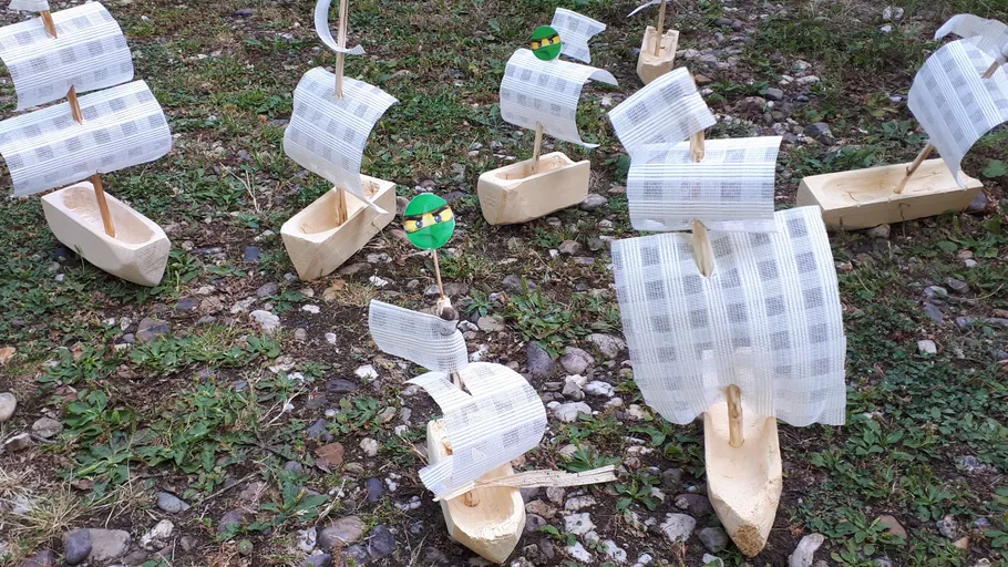 Wooden toy ships on grassy and rocky ground.