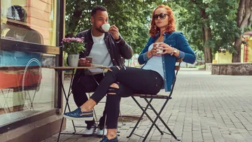 Two people drinking coffee at outdoor cafe.