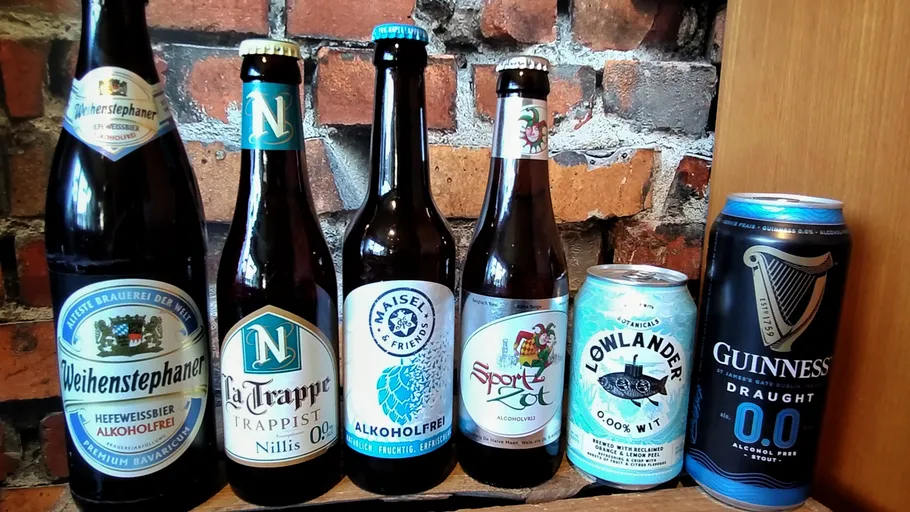 Six alcohol-free beer bottles on brick wall shelf.