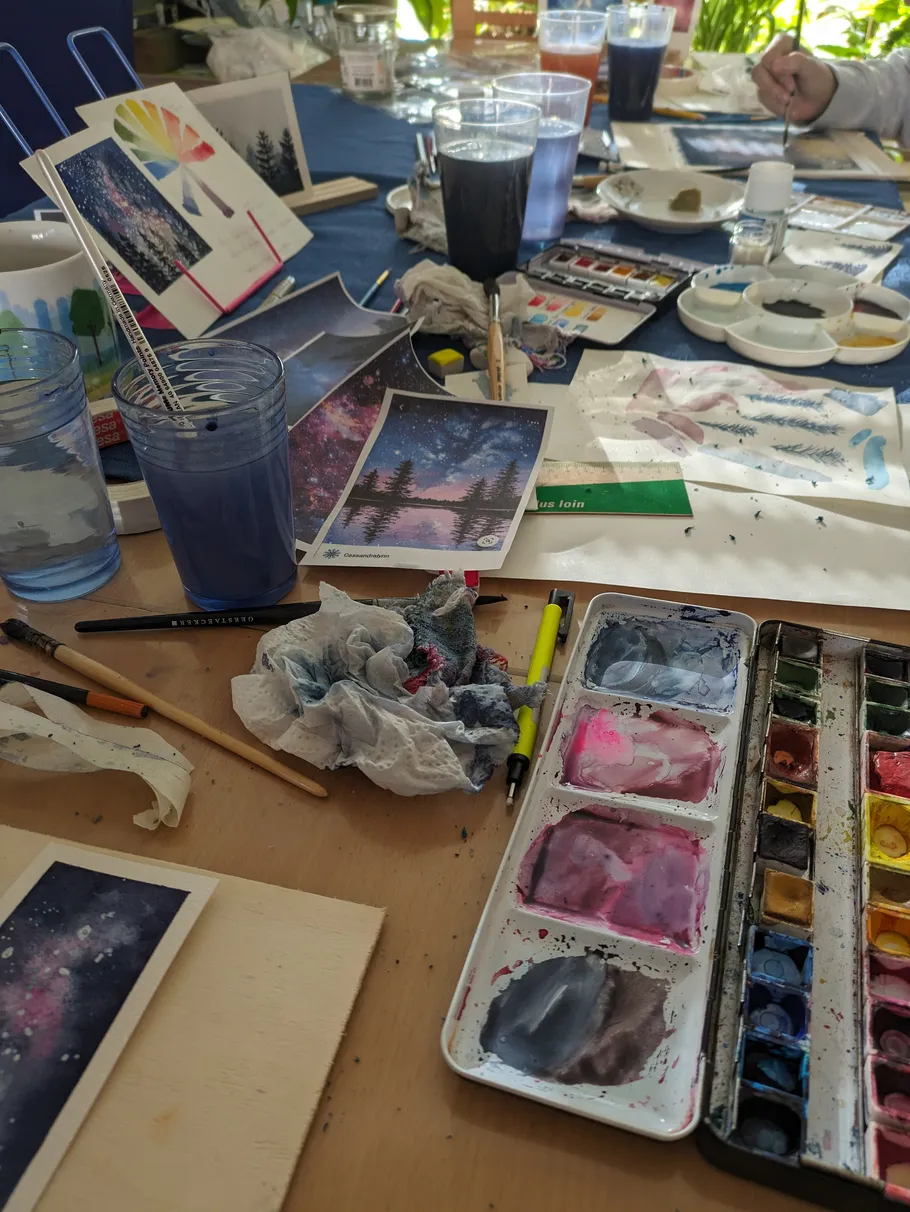 Künstlerischer Arbeitsplatz mit Aquarellbedarf und Gemälden.