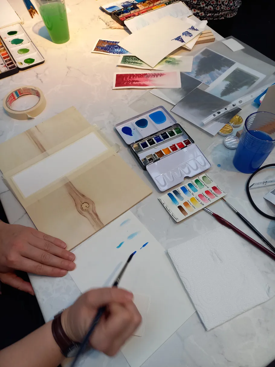 Person painting with watercolors on a table.