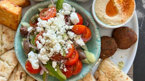 Greek salad surrounded by pita, hummus, and falafel.
