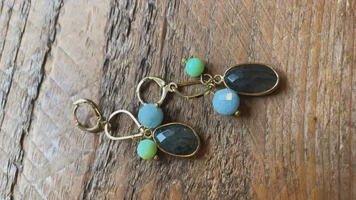 Gold earrings with blue and green stones on wood.