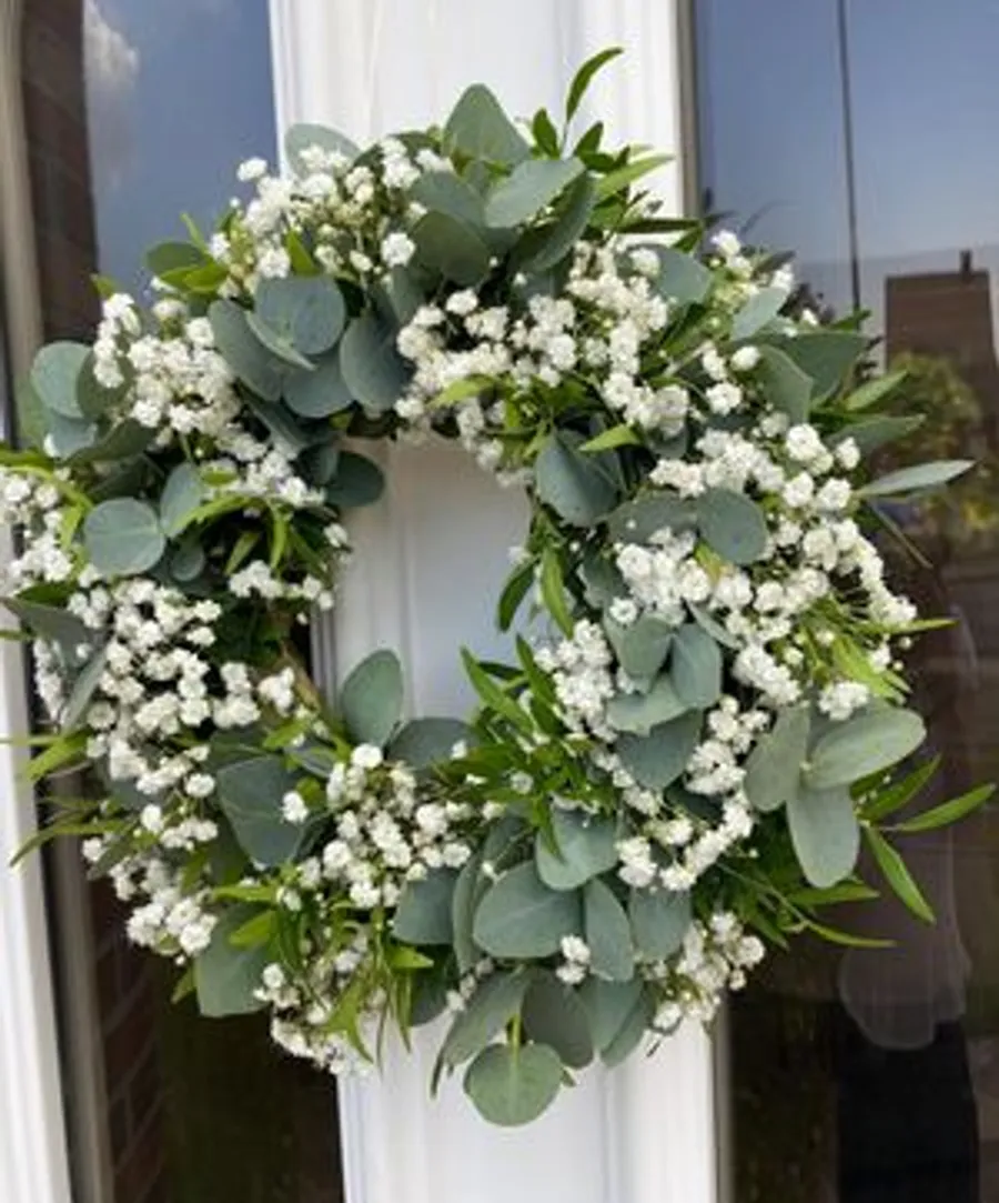 Kranz mit weißen Blumen an Tür.